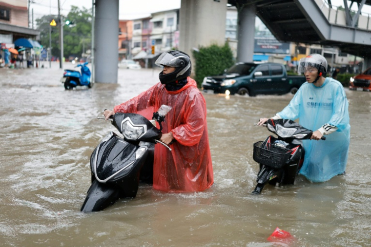 Des personnes poussent leurs motos à travers les eaux de crue dans le district de Bang Bua, à Bangkok, le 26 septembre 2026 ( AFP / WIKUS DE WET )