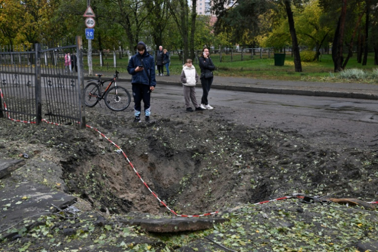 Des personnes se tiennent près d'un cratère causé par un missile, à proximité d'une école endommagée à la suite d'une attaque russe à Kiev, le 19 octobre 2026 ( AFP / Sergei SUPINSKY )
