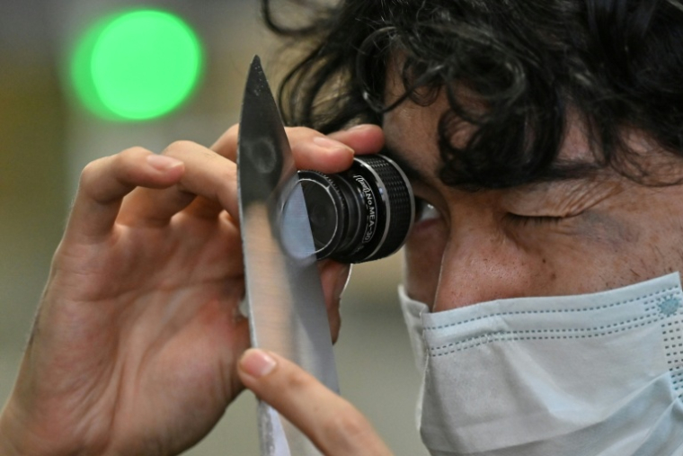 Un employé du fabricant japonais de couteaux Sumikama inspecte une lame à l'aide d'une loupe dans son usine de Seki, au Japon, le 22 juillet 2025 ( AFP / Richard A. Brooks )