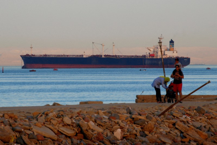 Des gens marchent sur la plage alors qu'un porte-conteneurs traverse le golfe de Suez en direction de la mer Rouge à Ain Soukhna