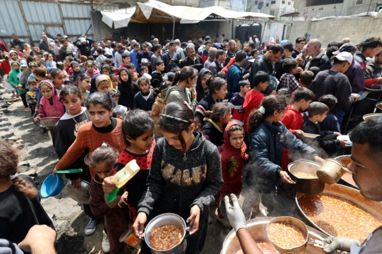 Des Palestiniens lors d'une distribution gratuite de nourriture dans le camp de réfugiés de Nuseirat, dans le centre de la bande de Gaza, le 12 avril 2025 ( AFP / Eyad BABA )