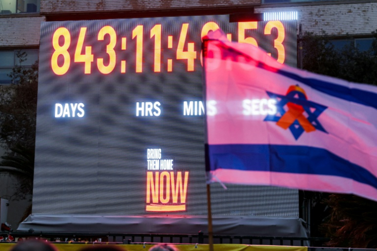 Un drapeau israélien orné d'un ruban jaune devant l'horloge comptabilisant les jours, les minutes et les secondes écoulées depuis l'enlèvement d'otages israéliens vers la bande de Gaza lors des attaques du 7 octobre 2023, à Tel-Aviv, le 27 janvier 2026 ( AFP / Jack GUEZ )