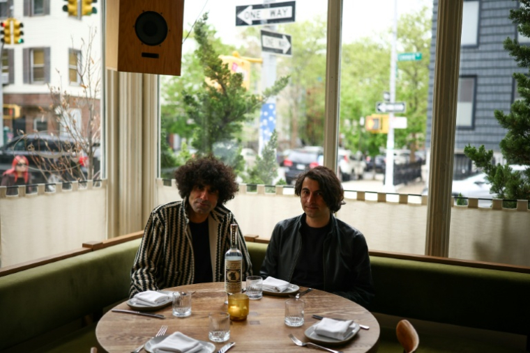 Siavash Karampour (à gauche) et Sasan Oskouei (à droite) posent avec une bouteille de leur eau-de-vie traditionnelle iranienne, l'aragh sagi, dans un restaurant de Brooklyn à New York, le 28 avril 2026 ( AFP / CHARLY TRIBALLEAU )