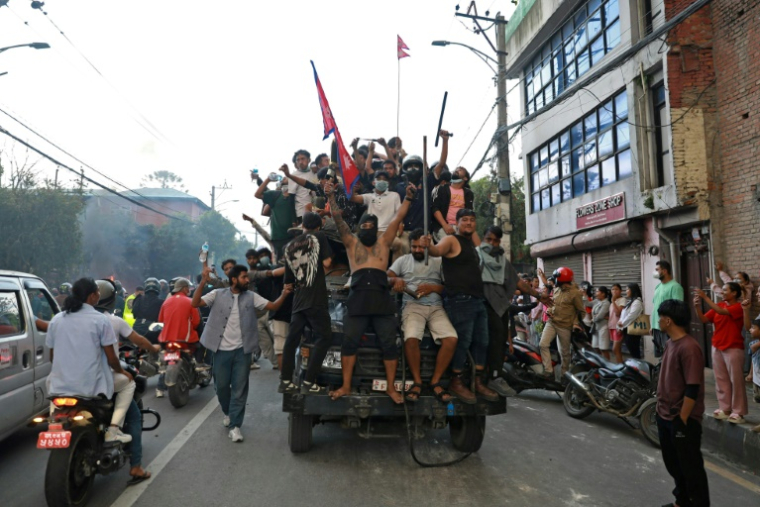 Des manifestants montés dans un camion de la police, portent le drapeau national du Népal devant la Maison du Président à Katmandou, le 9 septembre 2025 ( AFP / Prabin RANABHAT )