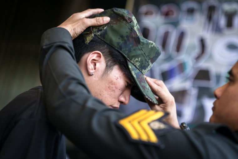 Un soldat thaïlandais met une casquette militaire sur la tête d'une nouvelle recrue, à la suite d'une loterie le 7 avril 2026 à Bangkok ( AFP / chanakarn LAOSARAKHAM )