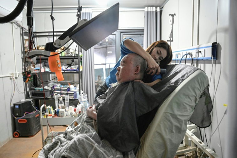 Li Xia, tétraplégique, est aidé par sa soeur Li Qian, chez eux, à Chongqing, en Chine, le 16 décembre 2025 ( AFP / Jade GAO )