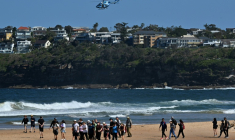 Des habitants marchent sur une plage de Sydney fermée à la suite d’une attaque de requin à Long Reef Beach tandis qu'un hélicoptère survole la zone, le 6 septembre 2025. ( AFP / Saeed KHAN )