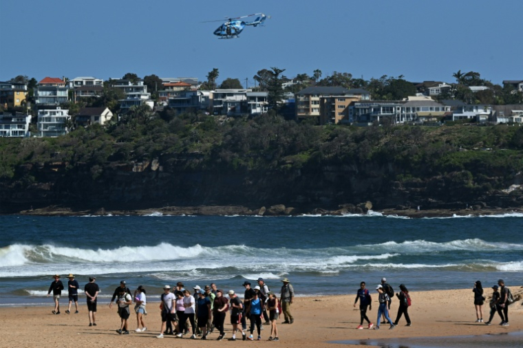 Des habitants marchent sur une plage de Sydney fermée à la suite d’une attaque de requin à Long Reef Beach tandis qu'un hélicoptère survole la zone, le 6 septembre 2025. ( AFP / Saeed KHAN )