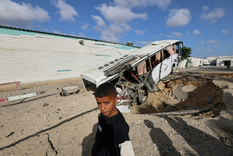 Un garçon se tient près d'un bus renversé et d'un cratère après une une frappe israélienne à Khan Younès, dans le sud de la bande de Gaza, le 14 mai 2025 ( AFP / Eyad BABA )