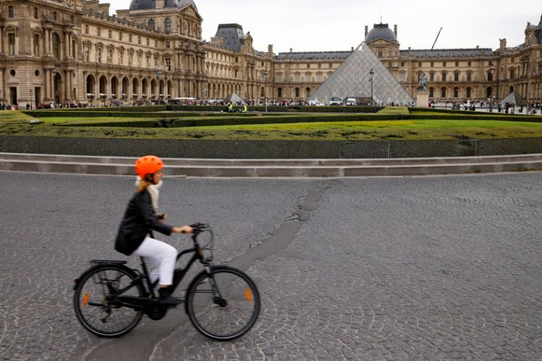 Une femme circule en vélo près de la pyramide du musée du Louvre à Paris