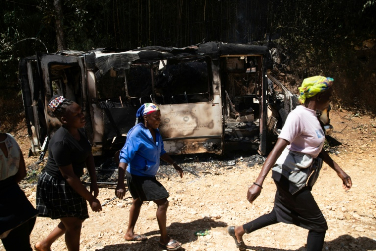 Des habitantes passent devant un véhicule calciné après des violences au cours desquelles plus de vingt personnes ont été tuées par des gangs armés à Kenscoff, près de Port-au-Prince, le 24 août 2026 en Haïti ( AFP / Clarens SIFFROY )