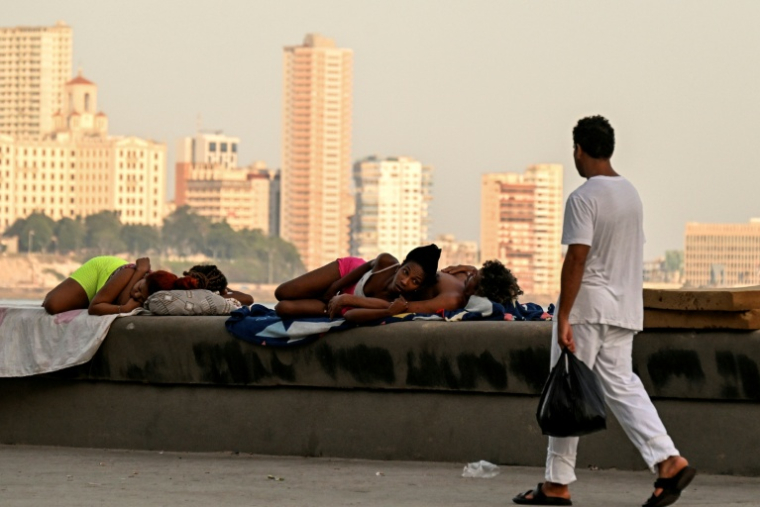 Un homme passe devant des femmes qui dorment sur le Malecon à La Havane lors d'une coupure de courant nationale, le 3 août 2026 ( AFP / YAMIL LAGE )