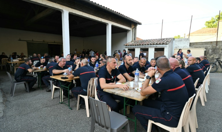 Les sapeurs-pompiers venus en renfort dans l'Aude lors d'un repas organisé en leur honneur à Talairan, dans l'Aude, le 8 août 2025 ( AFP / Bertrand GUAY )