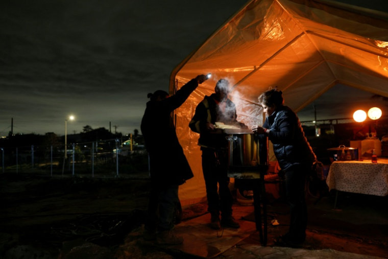 Un couple qui a perdu sa maison dans l'immense incendie de janvier 2025 cuisine une spécialité mexicaine sous une tente d'abri temporaire pour Noël, le 23 décembre 2025 à Altadena, à l'approche de la "rivière atmosphérique" qui doit traverser le sud de l'Etat cette semaine ( GETTY IMAGES NORTH AMERICA / MARIO TAMA )