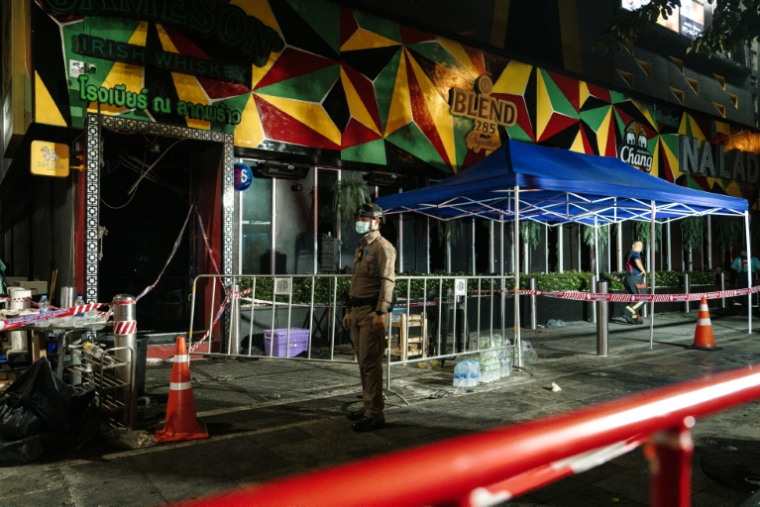 Un policier devant le bar Rong Beer Na Lat Phrao où s'est déclaré un incendie, le 13 juillet 2026 à Bangkok, en Thaïlande ( AFP / chanakarn LAOSARAKHAM )