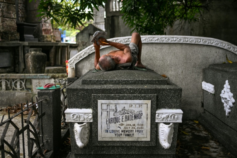 Un homme en train de résoudre des mots croisés sur une pierre tombale du cimetière nord de Manille, aux Philippines, le 21 octobre 2025 ( AFP / Jam STA ROSA )