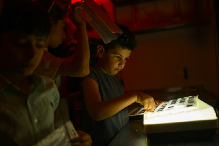 Des enfants regardent des pellicules photographiques dans une chambre noire lors d'un atelier organisé dans le cadre du projet "Fotohane Darkroom" à Mardin, dans le sud-est de la Turquie, le 14 juin 2026 ( AFP / Yasin AKGUL )