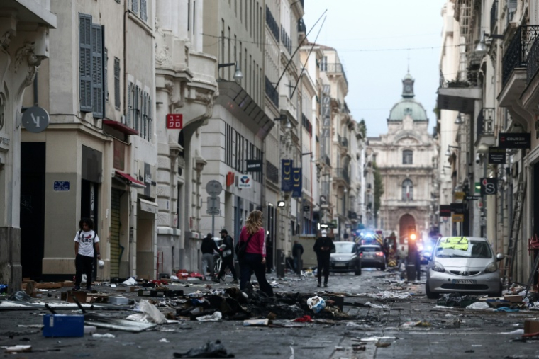 Des piétons dans une rue jonchée de débris au lendemain de manifestations contre la vie chère, le 18 octobre 2026 à Marseille ( AFP / Thibaud MORITZ )