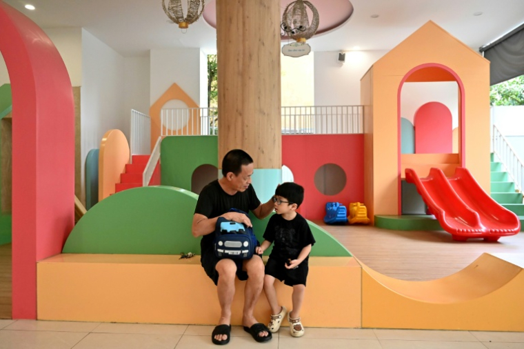 Un grand-père parle à son petit-fils près de jeux pour enfants, le 4 juin 2025 à Hanoï ( AFP / Nhac NGUYEN )