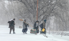 Des habitants marchent sous la neige avec leurs effets personnels sur une route de dans la province afghane de Parwan, dans l'est du pays, le 21 janvier 2026  ( AFP / Wakil KOHSAR )