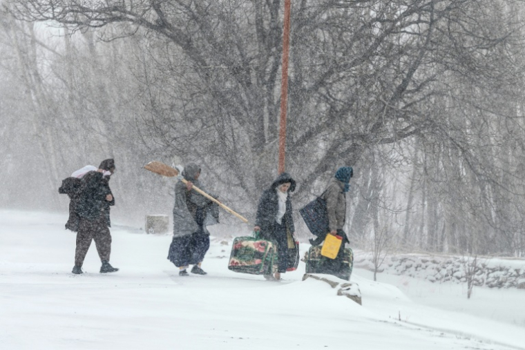 Des habitants marchent sous la neige avec leurs effets personnels sur une route de dans la province afghane de Parwan, dans l'est du pays, le 21 janvier 2026  ( AFP / Wakil KOHSAR )