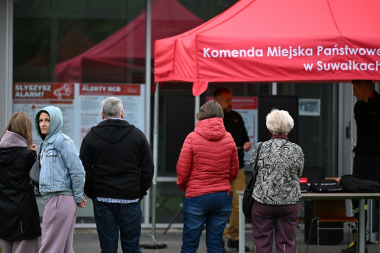 Des habitants écoutent un secouriste polonais expliquer les règles de conduite en cas d'alerte aérienne, lors d'une campagne de sensibilisation à Suwalki, près du corridor de Suwalki, le 26 septembre 2026. Le corridor de Suwalki est un tronçon de 104 kilomètres situé à la frontière entre la Pologne et la Lituanie, constituant la seule liaison terrestre entre les États baltes et le reste de l'Otan, tout en séparant le Bélarus de l'enclave russe de Kaliningrad. ( AFP / Sergei GAPON )