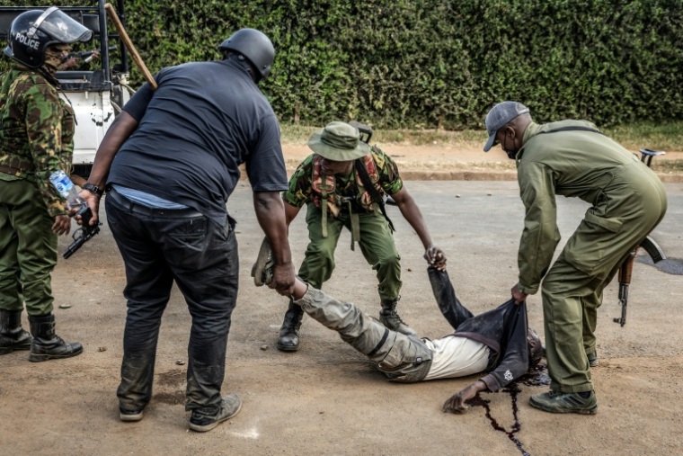 Des policiers transportent un manifestant grièvement blessé et inanimé lors d'affrontements au cours d'une manifestation contre un centre de quarantaine Ebola construit par les États-Unis sur la base aérienne de Laikipia, le 9 juin 2026 à Nanyuki, au Kenya ( AFP / Luis TATO )