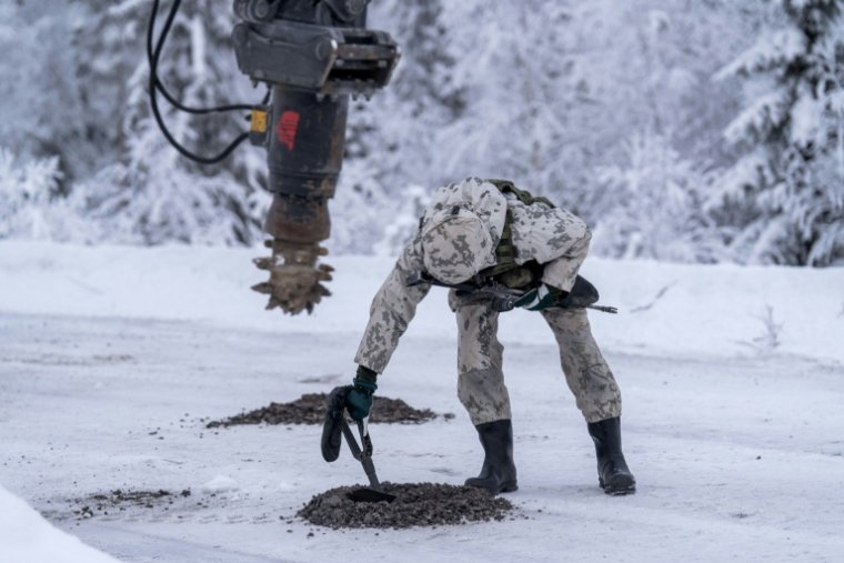 Un militaire finlandais à côté d'une excavatrice qui a creusé l’asphalte gelé pour enfouir des mines antichars d’exercice, à Kajaani, en Finlande, le 3 février 2026 ( AFP / Alessandro RAMPAZZO )
