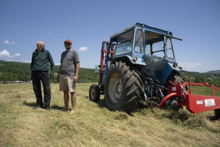 Emil Deliev, éleveur bulgare de 58 ans (G), et son fils Denislav Deliev, 29 ans, posent à côté d'un tracteur dans leur exploitation située près du village de Sofiytsi, dans la commune de Dzhebel, au sud-est de la Bulgarie, le 9 juin 2026 ( AFP / Nikolay DOYCHINOV )