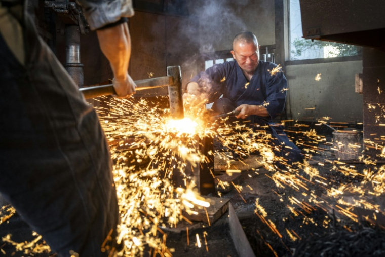 Le forgeron Akihira Kawasaki (d) maintient l'acier sur une enclume tandis que son apprenti Toru Watanabe martèle le métal pour forger des lames de katana, le 9 janvier 2026 à Misato, au Japon ( AFP / Yuichi YAMAZAKI )