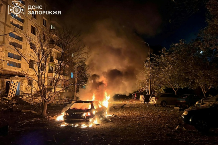 Photo prise et diffusée par les services d'urgence ukrainiens, le 5 octobre 2025, montrant une voiture en feu dans la cour d'un immeuble résidentiel après une attaque aérienne russe à Zaporijjia, en Ukraine ( Services d'urgence ukrainiens / Handout )