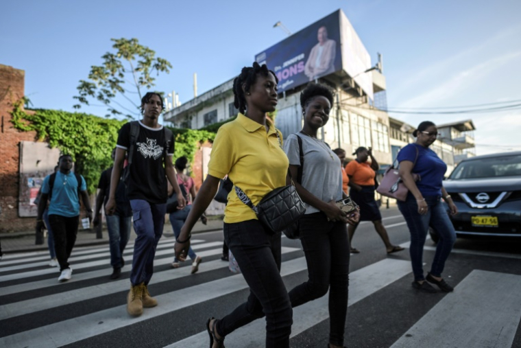 Des piétons sur un passage clouté à Paramaribo, capitale du Suriname couverte de panneaux de publicité électorale avant les législatives, le 23 mai 2025 ( AFP / Juan BARRETO )