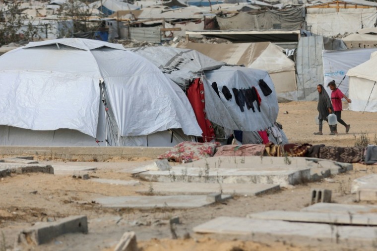 Des femmes palestiniennes transportent de l'eau dans un camp provisoire pour personnes déplacées installé dans un cimetière de Khan Younès, le 25 septembre 2025. ( AFP / Omar AL-QATTAA )