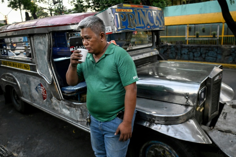 Le chauffeur de jeepney Eric Helera boit un café pendant une pause avant de prendre la route à Manille, le 23 mars 2026 ( AFP / Ted ALJIBE )