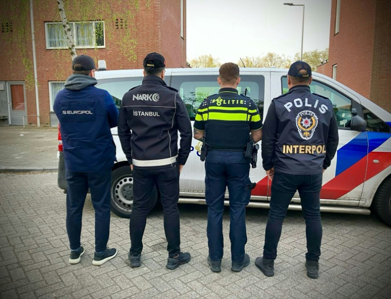 Cette photo, diffusée par la police néerlandaise le 15 avril 2025, montre des agents d'Europol, du Service de lutte contre les stupéfiants de la police d'Istanbul, de la police néerlandaise et de la division turque d'Interpol à côté d'un véhicule de police aux Pays-Bas ( DUTCH POLICE / - )