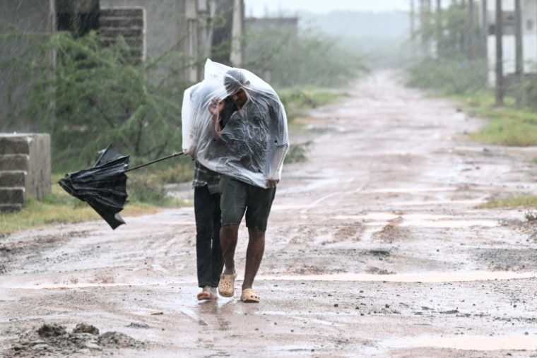 Des habitants se protègent de la pluie et du vent à Kakinada en Inde le 27 octobre 2026 avant l'arrivée du cyclone Arnab ( AFP / Noah SEELAM )