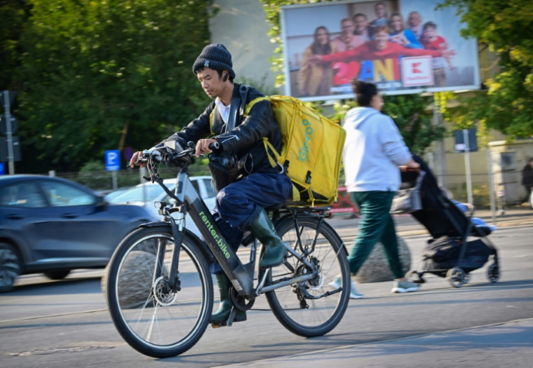 Un livreur de repas étranger circule à vélo dans une rue de Bucarest, le 10 octobre 2025 en Roumanie ( AFP / Daniel MIHAILESCU )