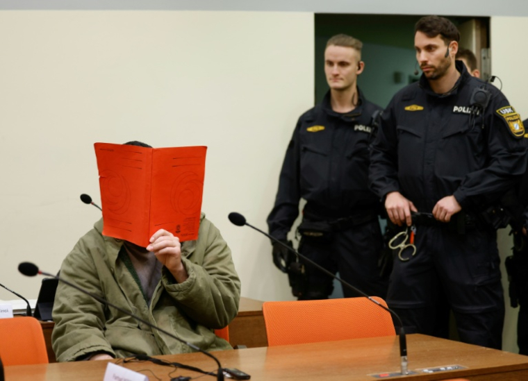 L'Afghan Farhad N. (g.), le visage caché derrière un dossier, est assis dans la salle d'audience du tribunal, le 16 janvier 2026 à Munich, pour le début de son procès pour avoir foncé en voiture dans la foule à Munich en 2025 ( AFP / Michaela Stache )