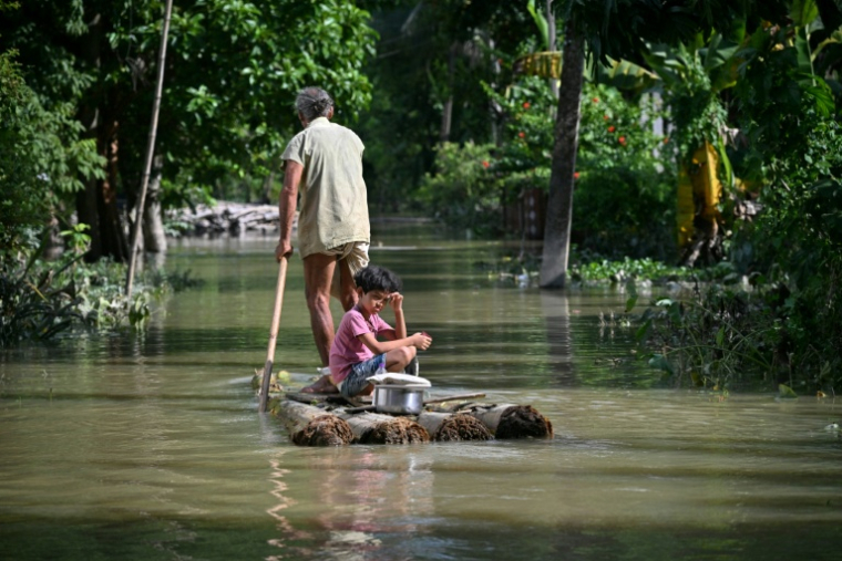 Un homme et une fillette  à bord d'un radeau de fortune,  sur une rivière en crure après des pluies de mousson torrentielles, dans un village du district de Sivasagar, dans l'Assam, en Inde,le 27 juillet 2026. ( AFP / Biju BORO )