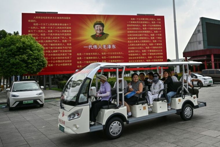 Des touristes à bord d'une voiturette électrique passent devant une fresque de Mao Zedong, place de "L'Orient est route", à Nanjie, dans la province du Henan, le 20 août 2026 en Chine ( AFP / Pedro PARDO )