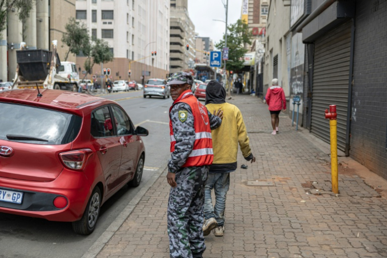 Un agent de sécurité repousse un sans-abri d'un trottoir du quartier central des affaires de Johannesburg, le 7 novembre 2025.  ( AFP / EMMANUEL CROSET )