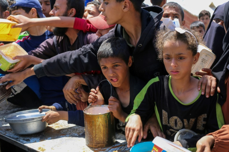 Des enfants palestiniens font la queue pour obtenir un repas chaud lors d'une distribution assurée par une cuisine soldiaire au camp de réfugiés de Nousseriat, dans le centre de la bande de Gaza, le 5 mai 2025 ( AFP / Eyad BABA )