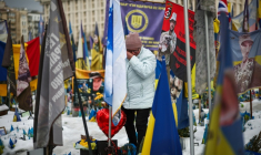 Un homme se recueille parmi les drapeaux et les fleurs d'un mémorial dédié aux soldats ukrainiens et étrangers tombés au combat, sur la place de l'Indépendance à Kiev, le 24 février 2026 ( AFP / HENRY NICHOLLS )