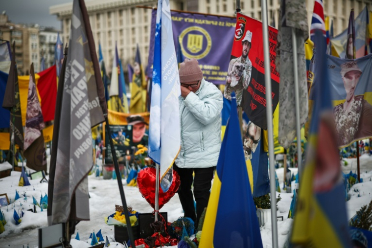 Un homme se recueille parmi les drapeaux et les fleurs d'un mémorial dédié aux soldats ukrainiens et étrangers tombés au combat, sur la place de l'Indépendance à Kiev, le 24 février 2026 ( AFP / HENRY NICHOLLS )