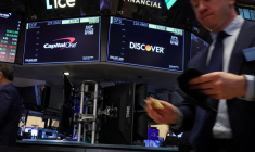 Des écrans affichent les logos et les informations sur les transactions de Capital One Financial et de Discover Financial pendant que les traders travaillent sur le parquet de la Bourse de New York