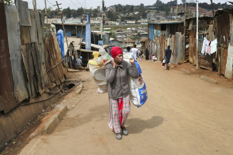Magret John porte un sac de déchets plastiques usagés vers un point de collecte de l'ONG Human Needs Project (HNP) dans le bidonville de Kibera, à Nairobi, le 11 août 2025 au Kenya ( AFP / Tony KARUMBA )