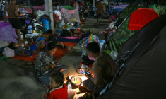Une famille déplacée par les combats prend un repas en s'éclairant avec une lambe de poche dans un camp de la province de Banteay Meanchey, au Cambodge, le 12 décembre 2025 ( AFP / TANG CHHIN Sothy )