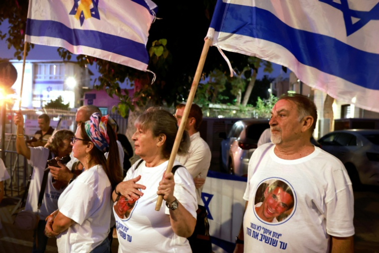 Des Israéliens portant des t-shirts serties de l'image du soldat Hadar Goldin attendent l'arrivée de sa dépouille devant le centre médico-légal national à Tel-Aviv le 9 novembre 2025.  ( AFP / Menahem Kahana )