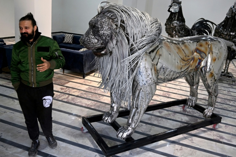 Le sculpteur Ehtisham Jadoon à côté de sa création, un lion à la crinière d'acier torsadé réalisé à partir de ferraille, dans son atelier situé à la périphérie d'Islamabad, le 29 décembre 2025 au Pakistan ( AFP / Farooq NAEEM )