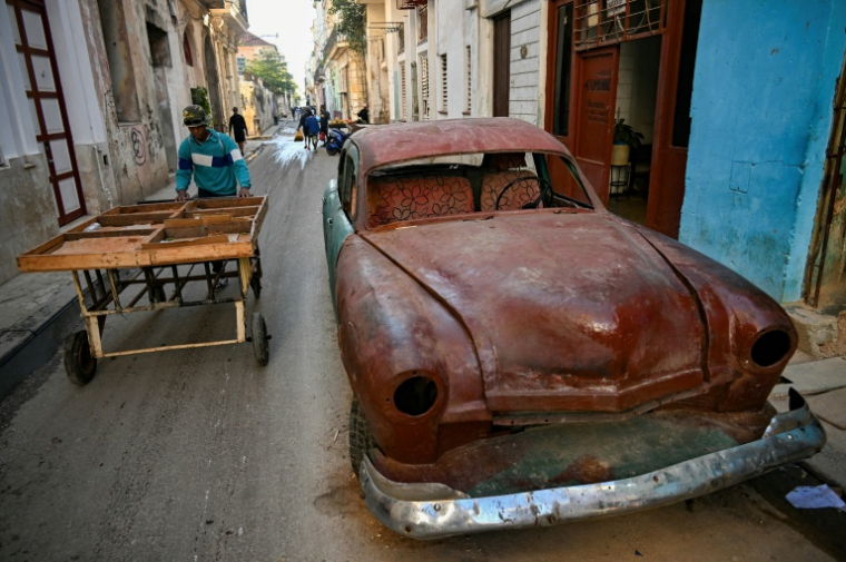 Un homme pousse une charrette près d'une vieille voiture dans une rue de La Havane, le 4 mai 2026 ( AFP / YAMIL LAGE )